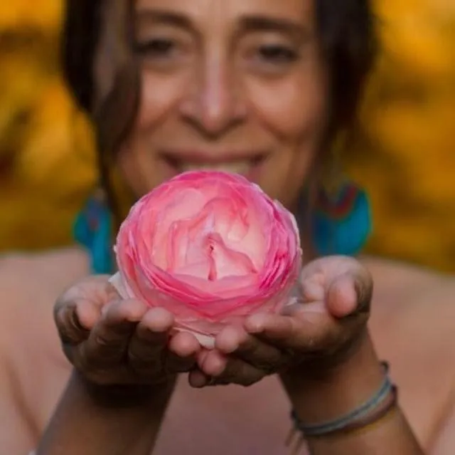 Claudia Aguirre tend vers l'objectif une rose pâle posée au creux de ses deux mains ; derrière elle, un feuillage doré flou.